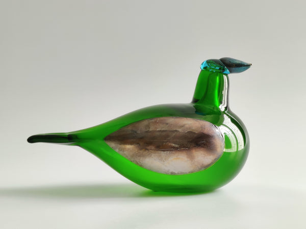 A hand-blown glass bird figurine with a vibrant green body, a textured brown and beige wing, and a small blue beak, shown on a neutral light gray background.