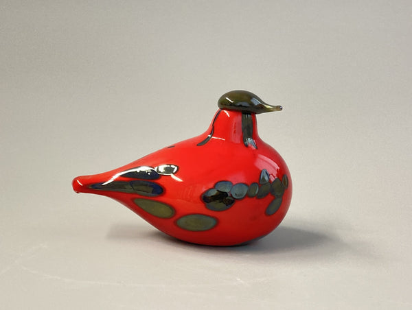 Red glass bird ornament with black and gold details on a gray background
