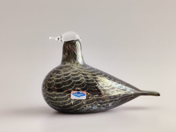 A decorative glass bird figurine with a dark iridescent body, shimmering silver and green patterns, and a clear glass beak, shown against a neutral light gray background.