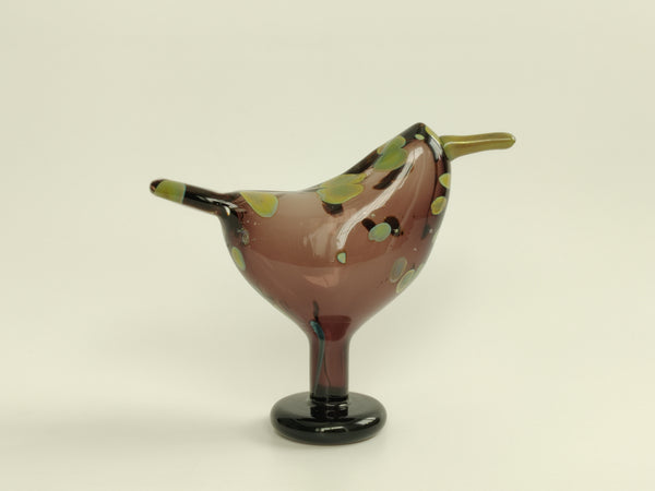 Glass bird figurine with brown, green, and black colors on a beige background